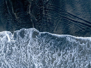 Aerial: Top down shot of Waves breaking on black sand beach