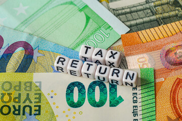 Small beads with text Tax Return on a pile of euro banknotes, closeup detail
