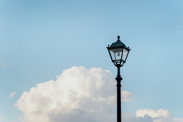 An elegant street lamp stands against a backdrop of lush clouds and a clear blue sky.