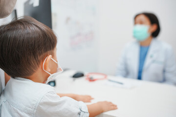 Fototapeta premium Child wearing mask visiting a masked doctor in a clinic. Medical consultation and health checkup during pandemic safety measures.
