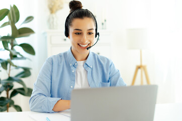 Sociable pretty arabian or indian woman, with headset, working as call center operator consulting...