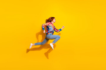 Full size photo of good mood girl dressed print shirt jeans running look at discount empty space isolated on yellow color background