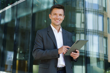 Businessman Using a Tablet While Standing Outside a Modern Office Building During Daytime in an Urban Setting