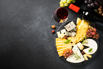 Cheese platter and red wine. Craft cheese set with grape on slate board. Top view at black background.