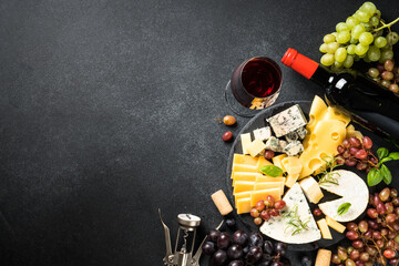 Cheese platter and red wine. Craft cheese set with grape on slate board. Top view at black background.