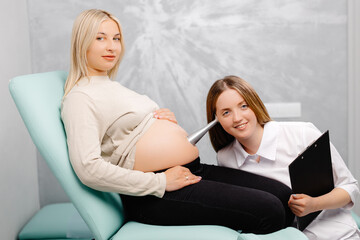 A gynecologist leans a stethoscope to a pregnant woman's belly and listens to the baby's heartbeat