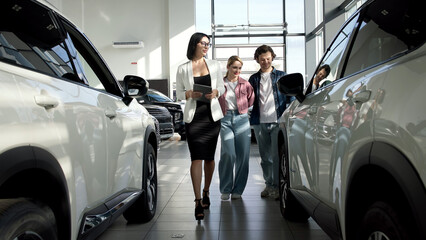 A female car dealer uses a digital tablet to assist clients in the showroom. She engages with...