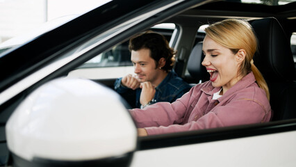 A happy young couple buys a family car in a modern dealership, excited about their new purchase. Their joy reflects the anticipation of new adventures and the importance of choosing the right vehicle.