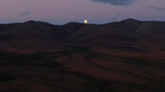 A Picturesque View of the Arctic Circle Showcasing a Tranquil Landscape Illuminated by a Glowing Moon at Night in Yukon, Canada - Wide Shot