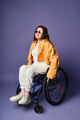 A young woman in trendy casual attire sits confidently in a wheelchair against a vibrant purple backdrop.