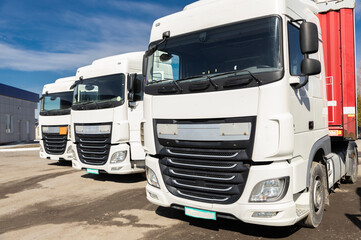 three trucks parked next to each other in a parking lot on a sunny day. view of the white cabs of tractor-trailers. Commercial vehicles, advertising of vehicles for business transportation
