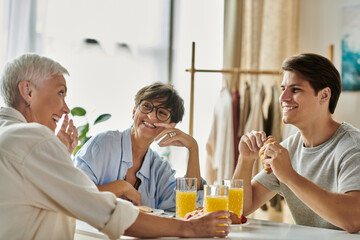 A gay couple enjoys a cheerful breakfast with their adult son, sharing laughs and delicious food.