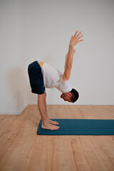 Caucasian Latino male in Ardha Uttanasana posture during a yoga session at home.