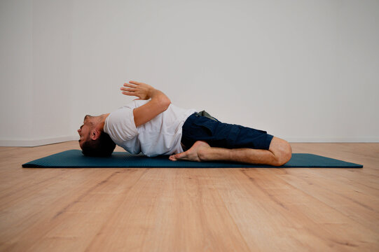Caucasian Latino male performing fish pose mudra (Matsyasana) in a home yoga session.