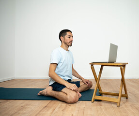 Caucasian Latino male performing a yoga session at home while following instructions from his...