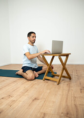 Caucasian Latino male performing a yoga session at home while following instructions from his...