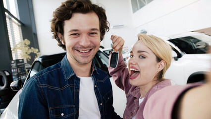 A happy young couple buys a family car in a modern dealership, excited about their new purchase. Their joy reflects the anticipation of new adventures and the importance of choosing the right vehicle.