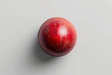 A weathered red cricket ball resting on a smooth gray surface, highlighting its intricate stitching and surface texture