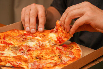 Tasty food at pizzeria. Concept of takeaway. Fast food order. Restaurant advertising. Delicious cheesy pizza. Pizza. Unhealthy food. Junk food. Fatty food. Hand taking pizza slice, close up view.