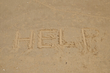 beach sand with the words HELP, concept of lost at sea needing help
