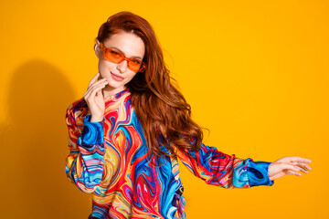 Photo of adorable gorgeous girl with foxy hairstyle dressed print shirt in sunglass touching cheek isolated on yellow color background