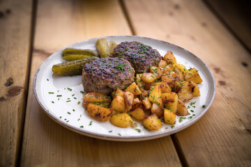 ready to eat - grilled venison burger, fried potatoes, pickles and chives served on a plate on a wood table