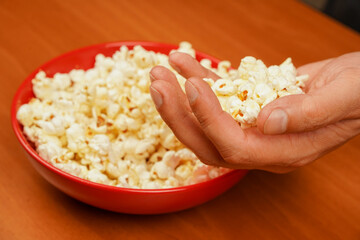 Fast food. Junk food. Snack for cinema. Flavored spicy popcorn scattered on table surface. Grabbing popcorn in hand. Delicious snack to eat in the cinema. Salted popcorn. Popcorn.