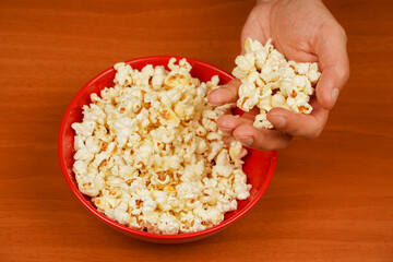 Popcorn. Fast food. Junk food. Snack for cinema. Flavored spicy popcorn scattered on table surface. Grabbing popcorn in hand. Delicious snack to eat in the cinema. Salted popcorn.