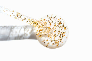 Luxurious skincare serum with gold flakes in clear glass dropper on white background