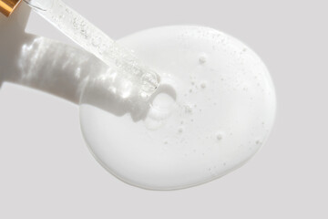 Clear liquid serum dropper with light reflections and texture on gray background for skincare and beauty concepts