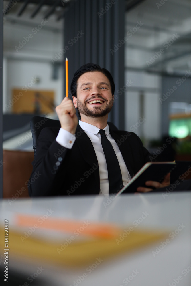 Poster a man in a suit is holding a pencil and smiling. he is sitting at a desk with a notebook and a ruler