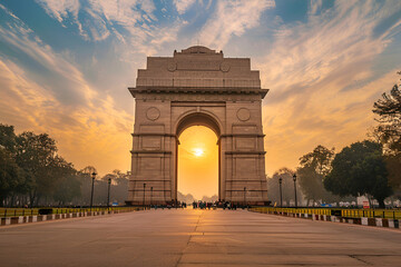 Majestic view of India Gate under a clear blue sky, symbolizing Delhi’s rich heritage and history. The iconic sandstone arch stands tall, surrounded by lush greenery and tourists.