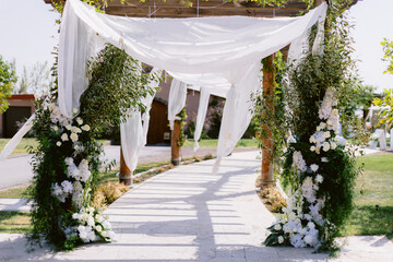 Elegant outdoor wedding arch adorned with white flowers and greenery under a sunny sky