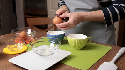 Process of making dough. Woman separates egg white from yolk in kitchen. Scales and eggs, utensils...
