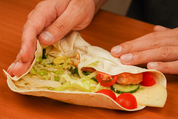 Fast food. Junk food. Eating. Food. Delicious. Cooking chicken roll. Tortilla wrap with fried chicken meat and vegetables, close up. Shawarma tomato, cucumber, onion, lettuce and chicken meat.