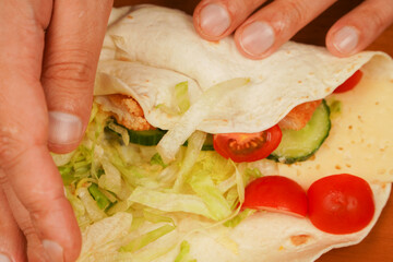 Fast food. Junk food. Eating. Food. Delicious. Preparing chicken roll. Tortilla wrap with fried chicken meat and vegetables, close up. Shawarma tomato, cucumber, onion, lettuce and chicken meat.