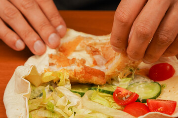 Fast food. Junk food. Eating. Food. Delicious. Preparing chicken roll. Tortilla wrap with fried chicken meat and vegetables, close up. Shawarma tomato, cucumber, onion, lettuce and chicken meat.