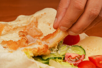 Cooking chicken roll. Tortilla wrap with fried chicken meat and vegetables, close up. Shawarma tomato, cucumber, onion, lettuce and chicken meat. Fast food. Junk food. Eating. Food. Delicious.