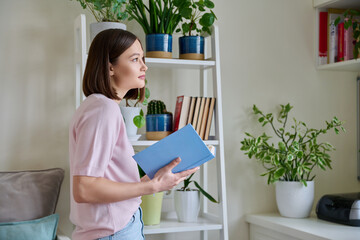 Happy smiling focused young woman reading book at home near window