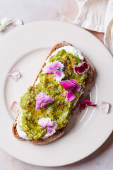 Breakfast avocado toast with pink culinary flowers, on pink marble background.