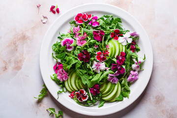 Green salad with apple and pink culinary flowers on plate, on pink marble background.