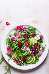 Green salad with apple and pink culinary flowers on plate, on pink marble background.