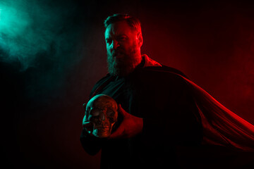 Photo of creepy cruel halloween character frightening man holds human skull isolated on dark misty...