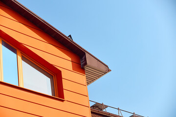 Wall of commercial building with large windows and orange metal ventilated facades made of Linear panels or facade cassettes. Fragment of building over blue sky with copyspace.
