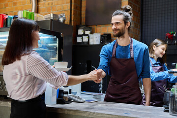Guy working in cafe with cup of coffee at bar counter serving female client