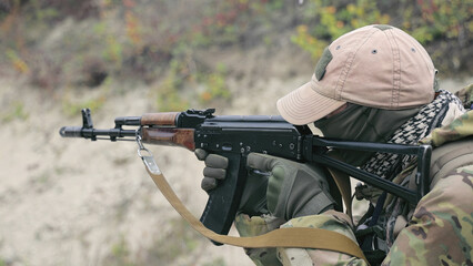 Soldier Aiming Rifle During Training. A soldier in camouflage gear and a tan cap aims a rifle...