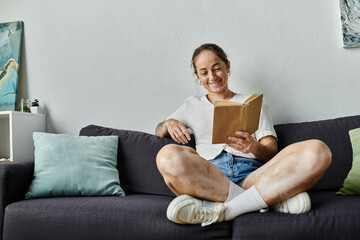 A woman with vitiligo smiles while enjoying a book in a comfortable setting.