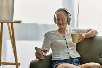 Relaxing indoors, a woman with vitiligo smiles while sipping a drink and using her phone.
