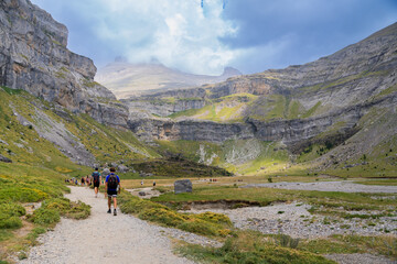 Obraz premium Hikers walking along a mountain trail with rocky cliffs and green valleys