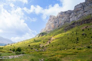 Fototapeta premium Sunlit mountain slope with green meadows and rocky cliffs